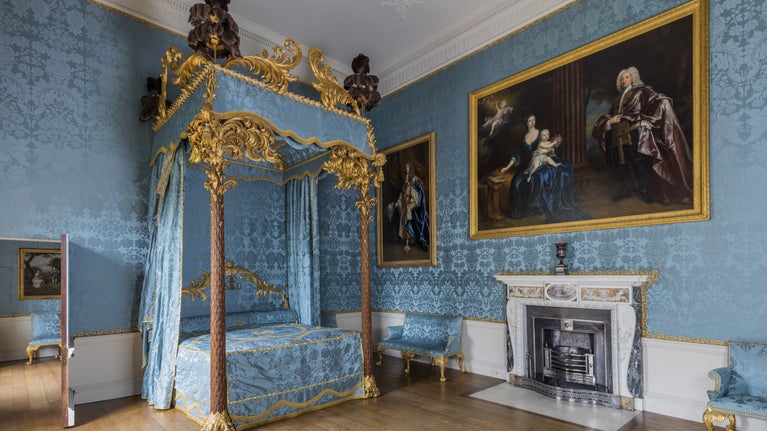 View of the blue and gold state bed and bedroom at Kedlestone Hall, with portraits to the right